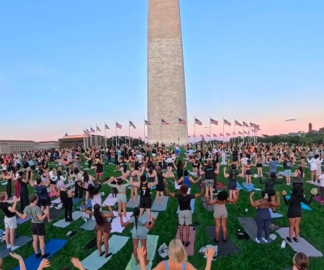 A crowd on yoga mats on the lawn beneath the Washington Monument at dusk